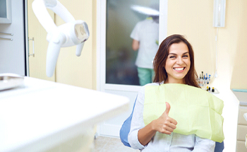 Smiling woman giving thumbs up after getting a dental checkup and teeth cleaning in Woodstock