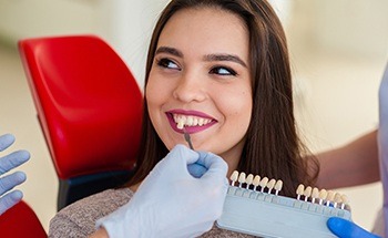 Woman in dental chair smiling with tooth color chart