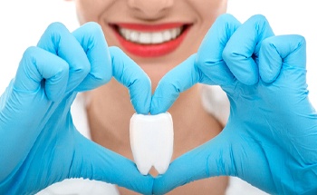 Dental team member making heart shape with hands with tooth model in middle