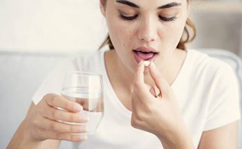 Woman taking white pill with water