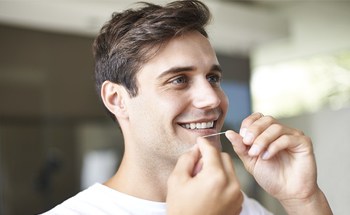 Man with bright smile flossing his teeth
