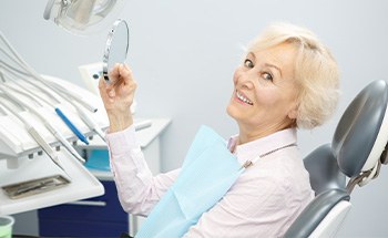 A smiling senior woman admiring her new dental bridge in a hand mirror